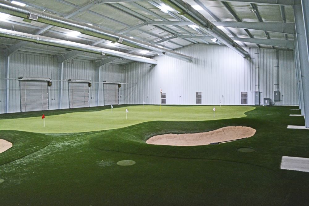 Custom indoor putting green installation featuring premium artificial turf, sand bunker, and multiple flagsticks inside a spacious metal training facility by Southwest Greens