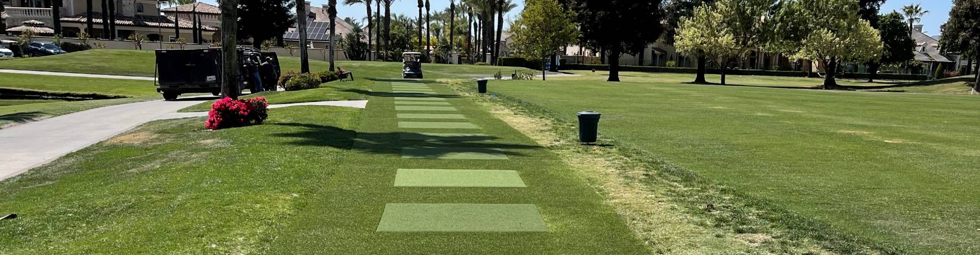Synthetic tee lines installed on a golf course driving range with alternating turf hitting mats, palm trees, and a residential golf community in the background